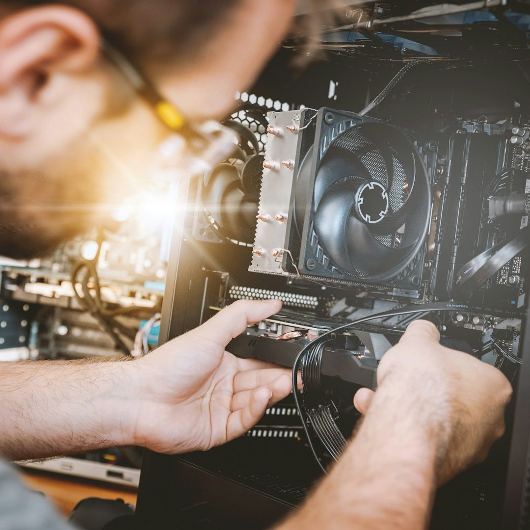 A person sitting with a computer tower, surrounded by various tech gadgets and neon lighting.